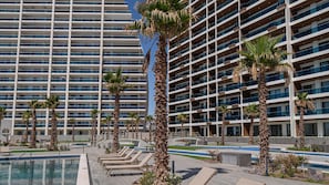 Ein modernes Hotel mit mehreren Etagen, einem Schwimmbad und Palmen.