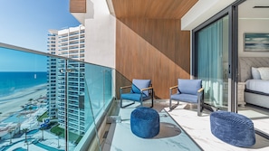 Ein Balkon mit Blick auf den Strand, zwei Stühle, eine Couch und ein großes Fenster.