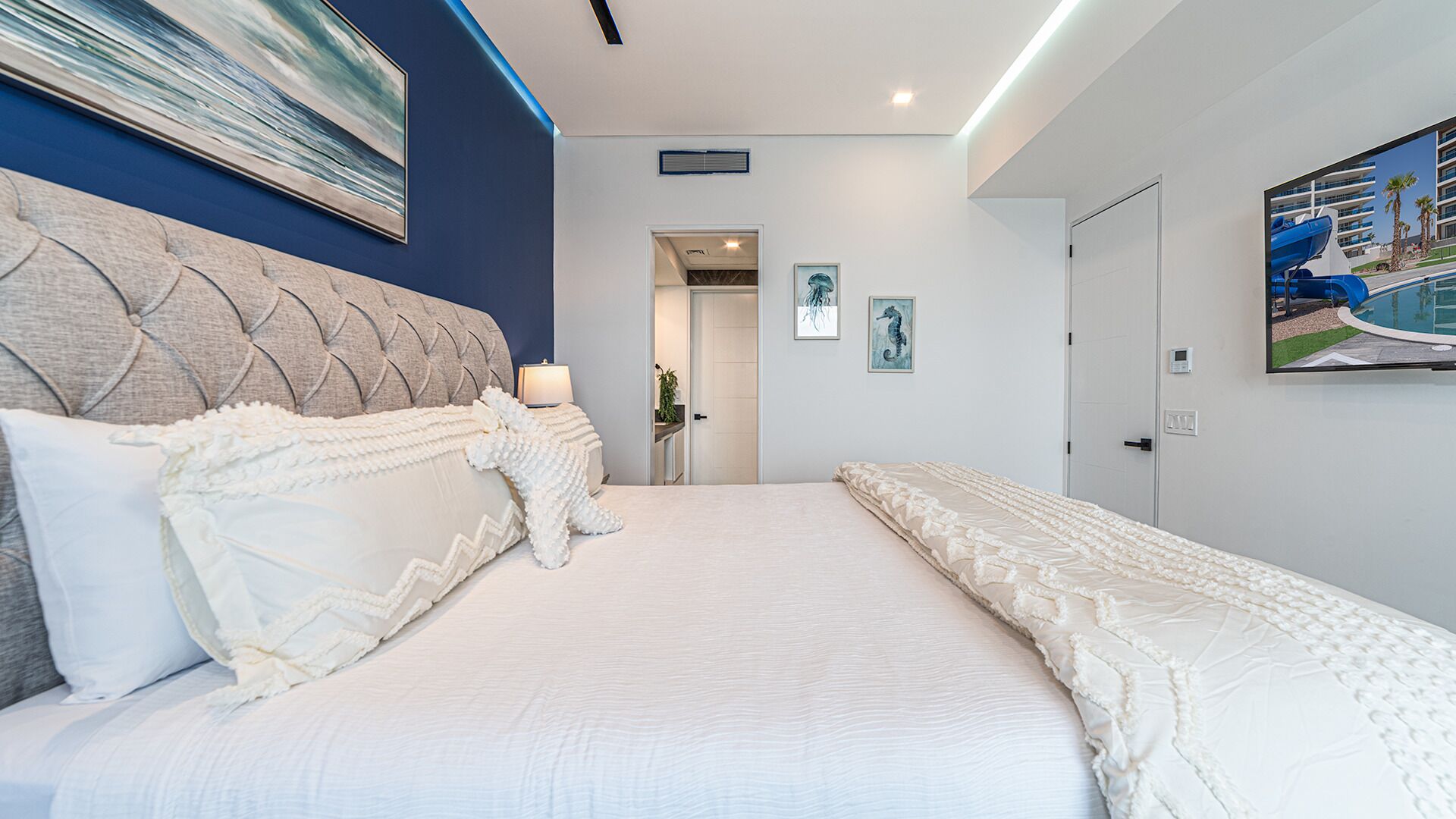 A modern bedroom with a large bed, a headboard, and a painting on the wall.