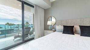 A hotel room with a large bed, a bedside table with a lamp, a view of the ocean, and a balcony with chairs. - R201 Luxury Oceanfront Retreat with Stunning Views and Spacious Modern Design (Puerto Peñasco)