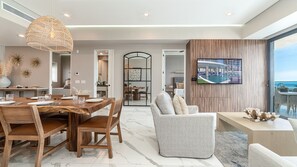 Uma sala de estar moderna com área de jantar, uma televisão grande na parede e vista para o oceano.