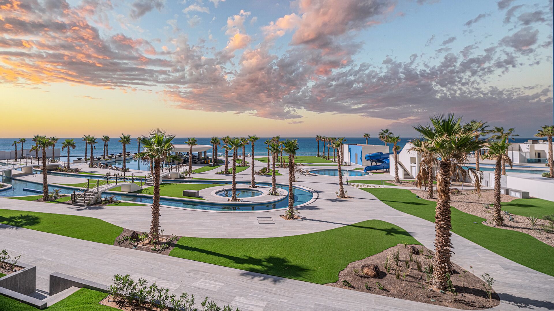 Un complexe hôtelier doté d’une piscine, de palmiers et offrant une vue sur l’océan au coucher du soleil.
