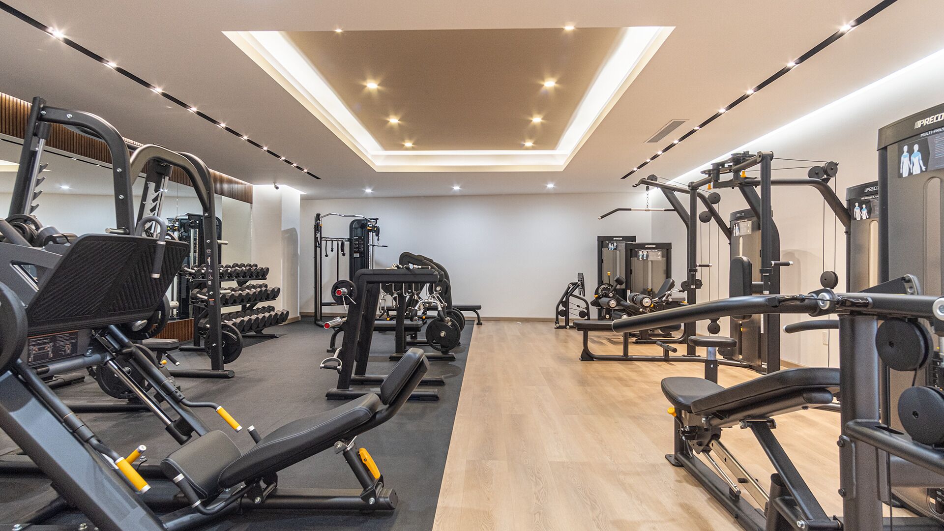 Ein Fitnessraum mit unterschiedlichen Trainingsgeräten, Holzboden und einer Dachfenster-Decke.