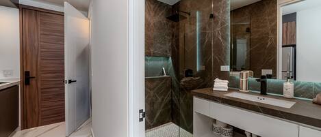 Un baño moderno con cabina de ducha de vidrio, tocador de mármol y un espejo grande.