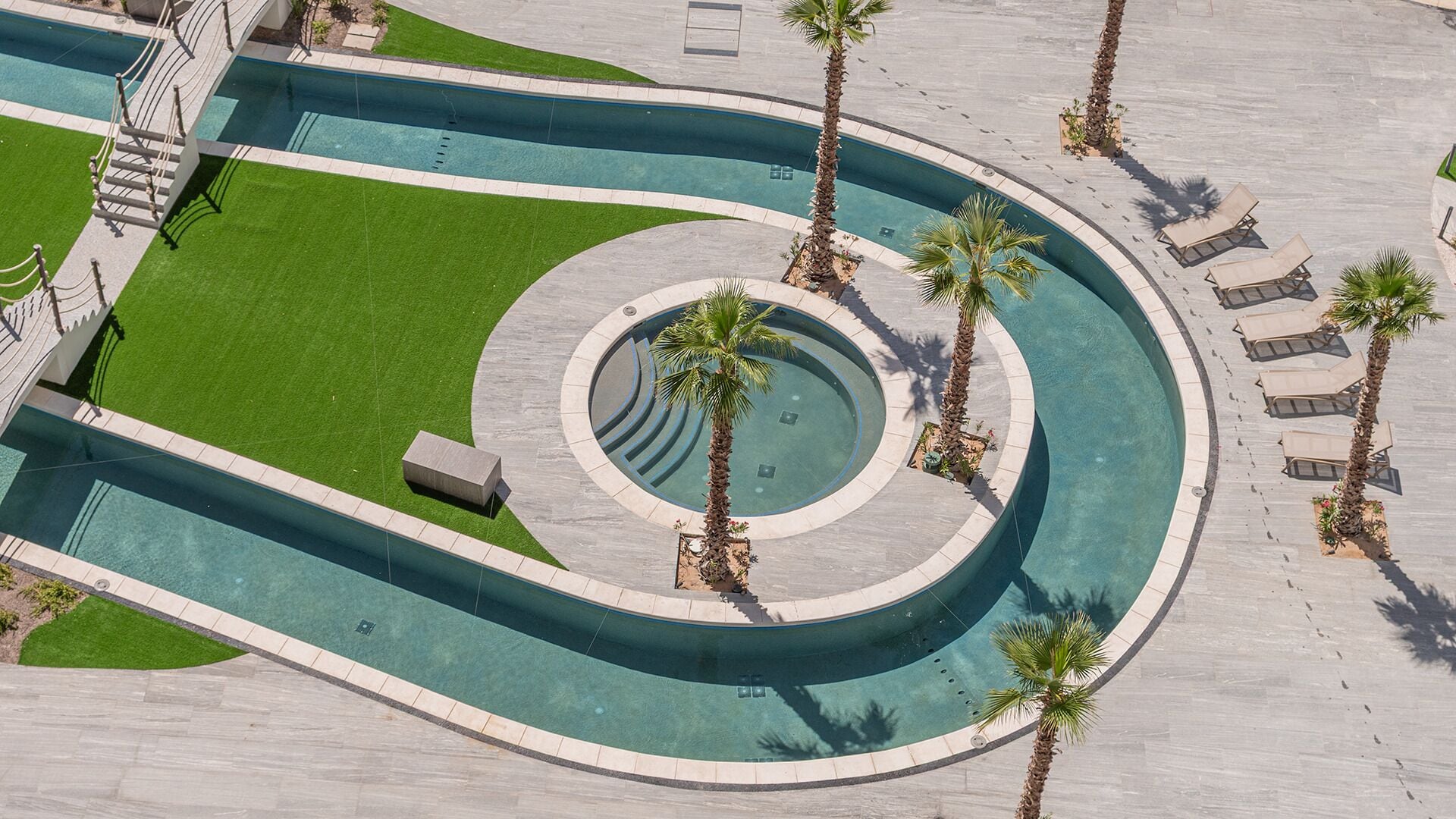 Ein Pool mit spiralförmigem Design, umgeben von Palmen und Liegestühlen.