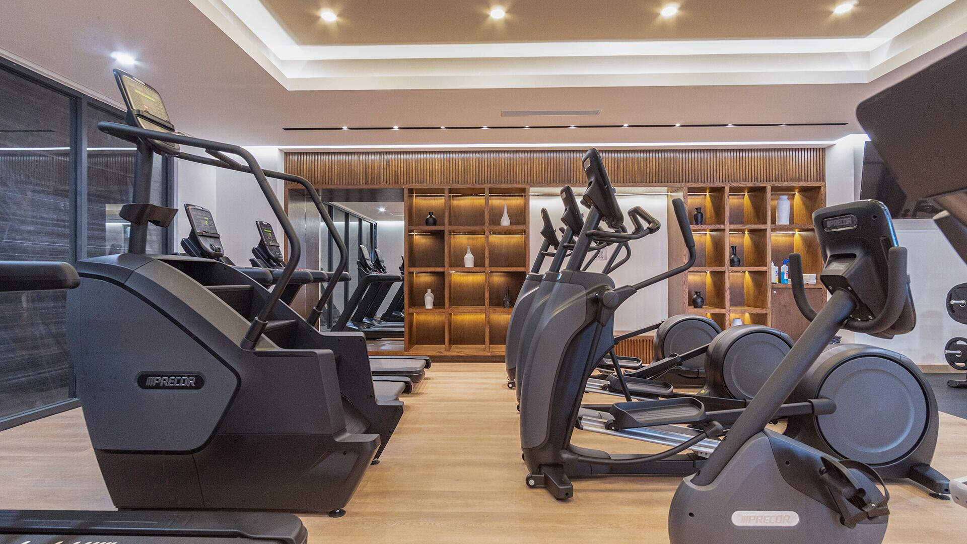 A gym with multiple treadmills and exercise bikes, wooden flooring, and a modern design.