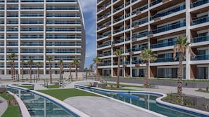 A modern hotel with multiple floors, outdoor pools, and palm trees. - R1701 Beachfront 3BR Condo with Dual Balcony Access & Spacious Open Living (Puerto Peñasco)