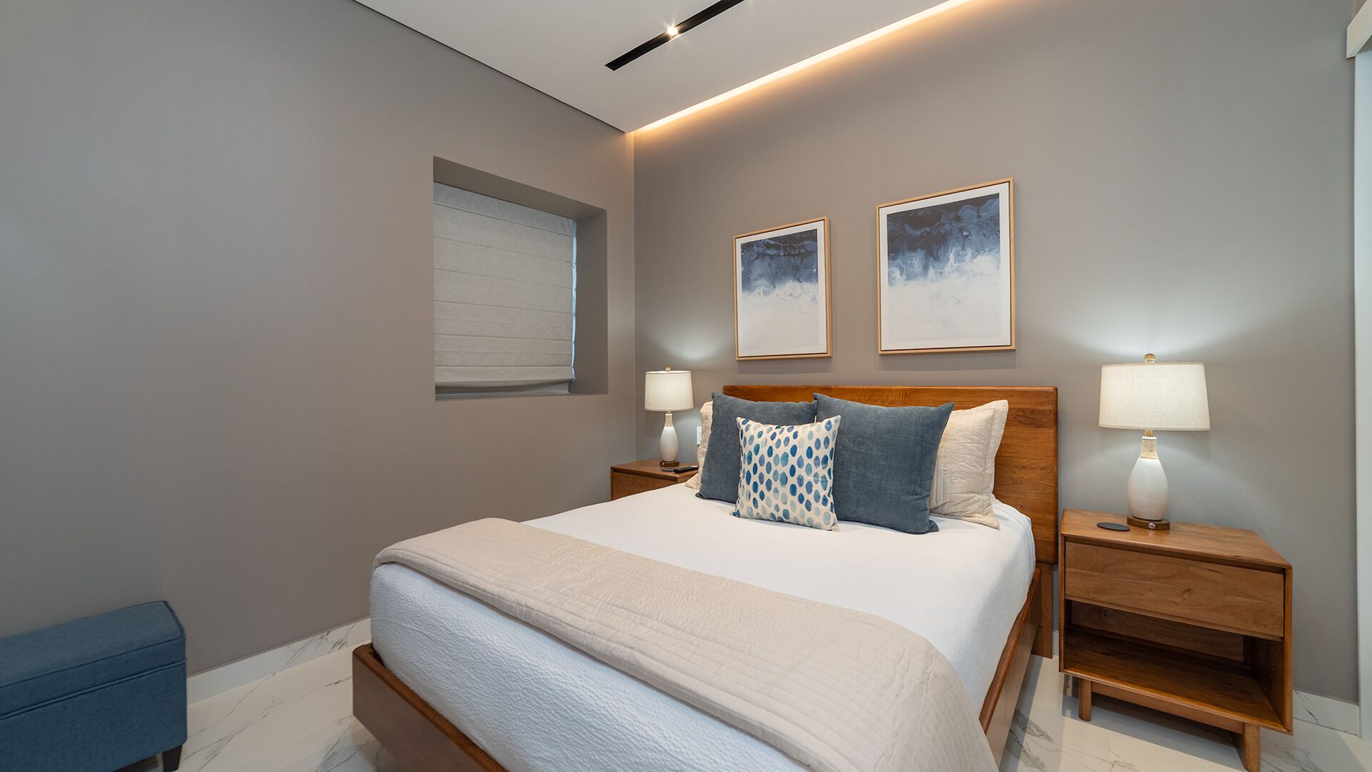 Een moderne slaapkamer met een groot bed, twee nachtkastjes, een raam met jaloezieën en twee ingelijste kunstwerken aan de muur.