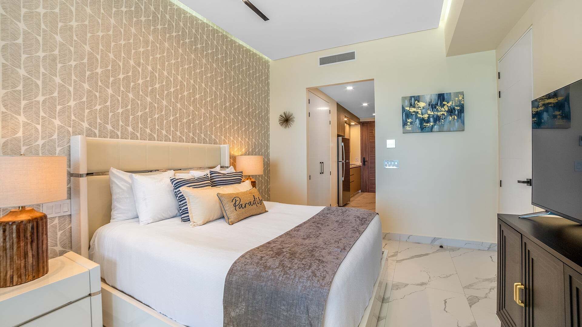A hotel room with a bed, bedside tables, a TV, and a bathroom visible through an open door.