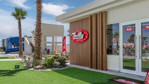 Ein modernes Gebäude mit einem 'Thrifty Ice Cream'-Schild, Palmen und einer blauen Rutsche.