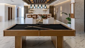 A pool table in a hotel lobby with marble flooring, wooden chairs, and pendant lighting. - R1805 | Modern 2BR Condo with Ocean Views & Private Balcony (Puerto Peñasco)