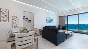 A modern living room with a sofa, dining table, and chairs, a balcony with a view of the sea, and artwork on the walls. - R1805 | Modern 2BR Condo with Ocean Views & Private Balcony (Puerto Peñasco)
