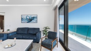 A modern living room with a large window offering a view of the sea, a blue sofa, a wooden chair, and a marble coffee table. - R1805 | Modern 2BR Condo with Ocean Views & Private Balcony (Puerto Peñasco)
