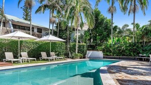 A swimming pool with lounge chairs and umbrellas, surrounded by palm trees and greenery. - Sea Crest- Unit 5, 47 Shirley St, The Crest Apartments (Byron)
