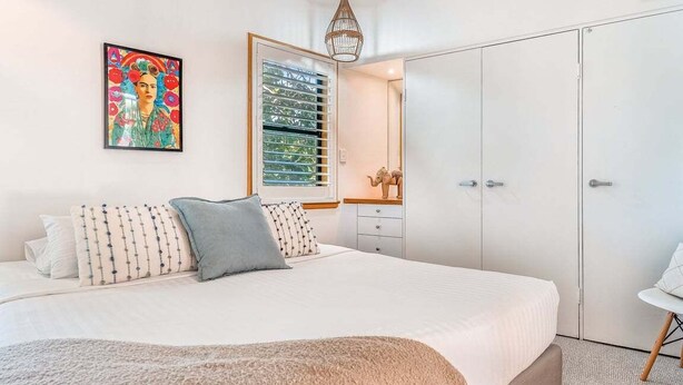 A bedroom with a bed, a bedside table, a wardrobe, a hanging light fixture, and a framed picture on the wall. - Sea Crest- Unit 5, 47 Shirley St, The Crest Apartments (Byron)