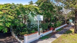 A small, white building with a sign indicating it is a hotel. It is surrounded by lush greenery and trees. - Sea Crest- Unit 5, 47 Shirley St, The Crest Apartments (Byron)
