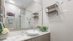 A modern bathroom with a large mirror, a white sink, and a shower area. - Luxury Oceanfront 2BR Maritima (Flamingos)