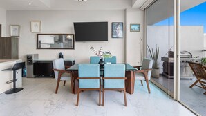 A modern dining area with a large table, chairs, and a flat-screen TV mounted on the wall. - Luxury Oceanfront 2BR Maritima (Flamingos)