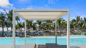 A poolside lounge area with a canopy, lounge chairs, and a wooden deck. - Luxury Oceanfront 2BR Maritima (Flamingos)
