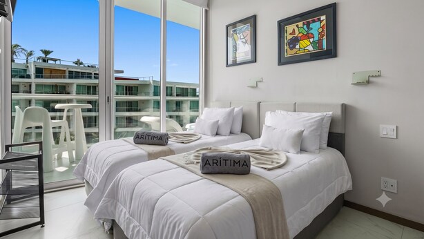 A hotel room with a large balcony, two beds with white bedding, and artwork on the walls. - Luxury Oceanfront 2BR Maritima (Flamingos)