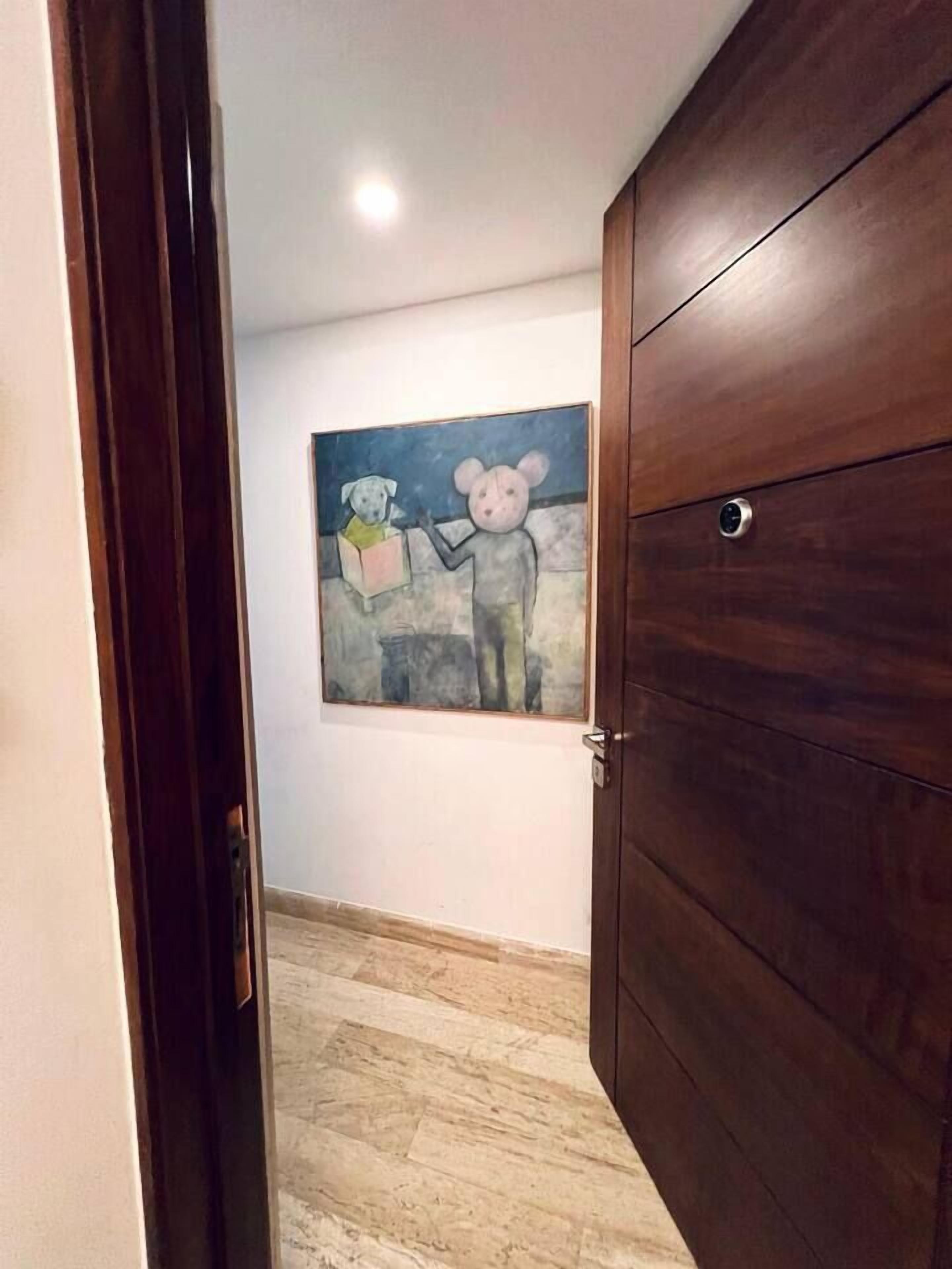 Un pasillo con puerta de madera, suelo de mármol y un cuadro en la pared.