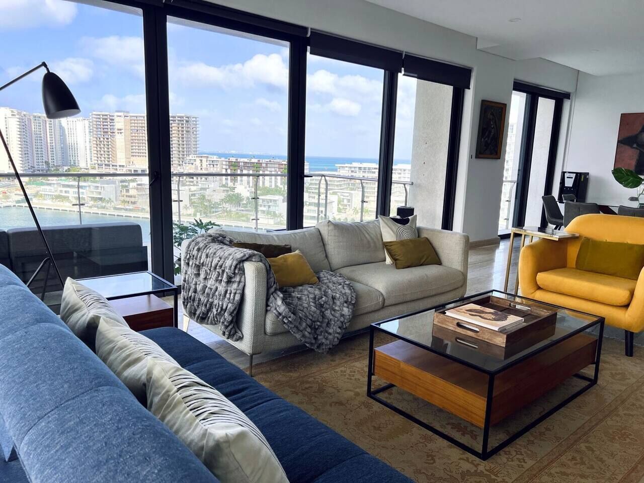 Un salon moderne comprenant un canapé, un fauteuil et une table basse, de grandes fenêtres offrant une vue sur la ville et un balcon.