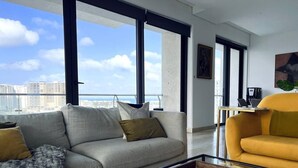 A modern living room with a sofa, armchair, and coffee table, featuring a large window with a city view. - TOP/4BR/Million Dlls Sea Views/4 Balcony/Padel/Gym (Cancún)