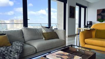 Ein modernes Wohnzimmer mit Sofa, Sessel und Couchtisch, mit einem großen Fenster und Blick auf die Stadt.