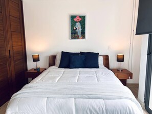 Una habitació d'hotel amb un llit gran, dues taules de nit amb làmpades, un armari de fusta i un quadre a la paret.