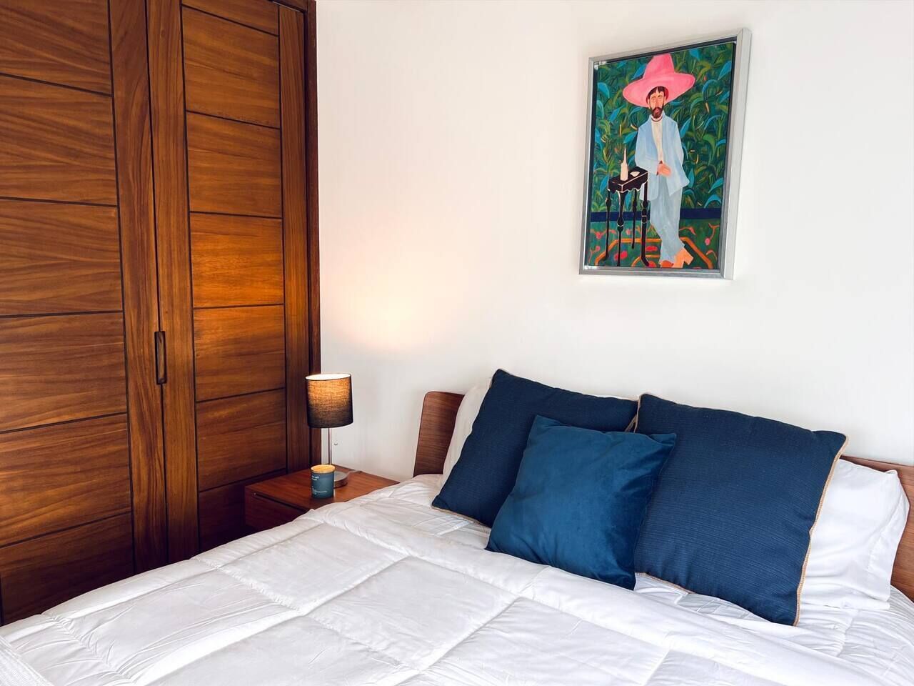 Ein Schlafzimmer mit Bett, Nachttisch, Lampe, Kleiderschrank und einem Gemälde an der Wand.