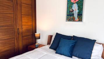 Un dormitorio con cama, mesita de noche, lámpara, armario y un cuadro en la pared.