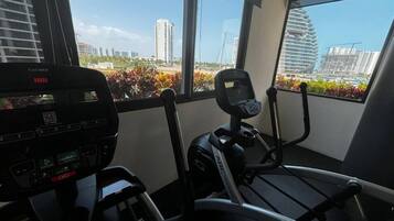 Ein Fitnessstudio mit Trainingsgeräten, großen Fenstern und Blick auf Gebäude.