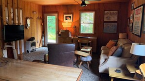 A cozy cabin interior with a wooden ceiling, a ceiling fan, a television, a desk with a chair, a couch, and framed pictures on the walls. - Spacious, waterfront privacy in Lake Leelanau , the heart of Leelanau County (Lake Leelanau)