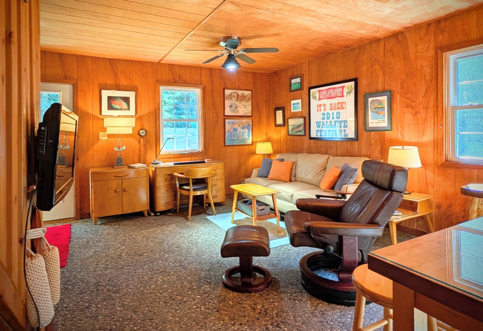 Una habitación acogedora con paredes de madera, un ventilador de techo, un sofá, un escritorio y una silla.