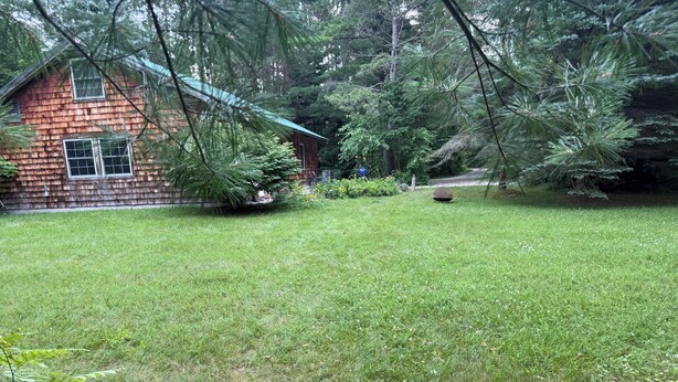 A wooden cabin with a well-maintained lawn and surrounding trees. - Spacious, waterfront privacy in Lake Leelanau , the heart of Leelanau County (Lake Leelanau)