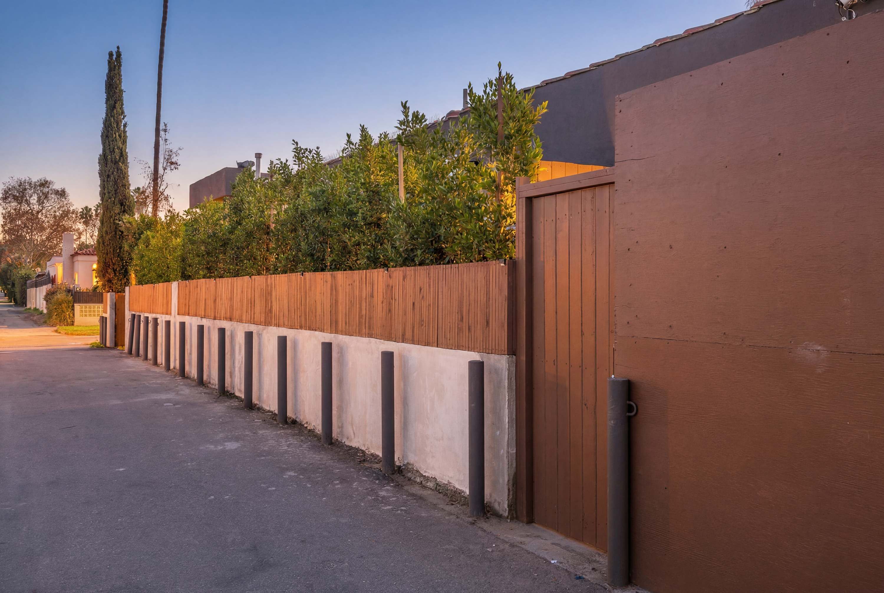 A residential street with a wooden fence, a concrete wall, and a gated entrance.