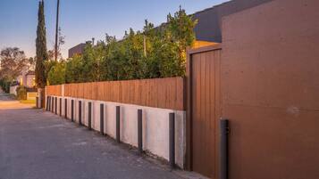 A residential street with a wooden fence, a concrete wall, and a gated entrance.