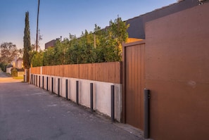 Una calle residencial con un cerco de madera, un muro de concreto y un acceso con portón.
