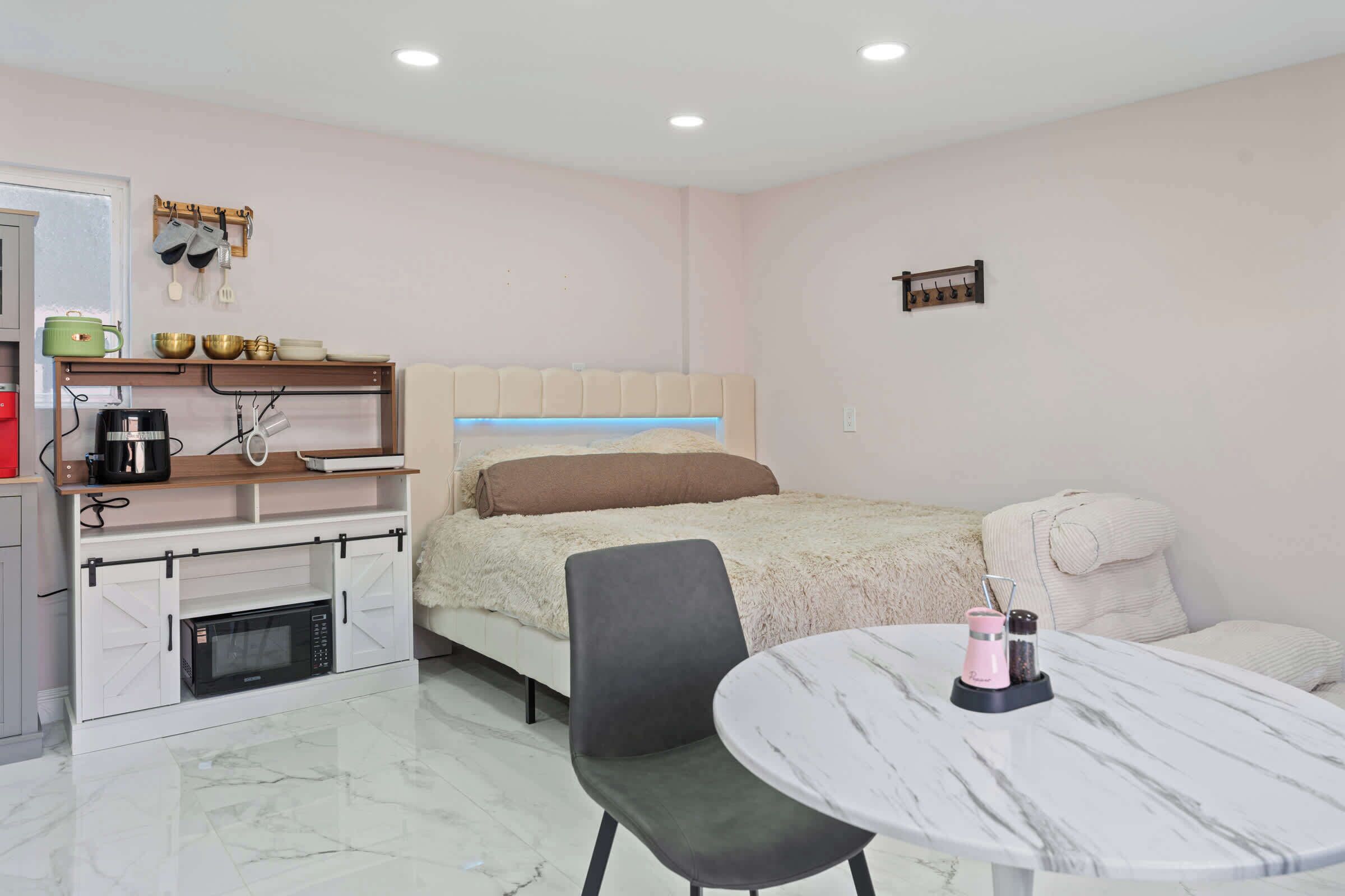 A compact hotel room with a bed, a desk with a computer, a chair, a small table, and a microwave.