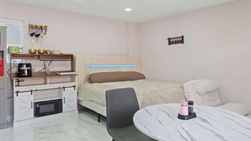A compact hotel room with a bed, a desk with a computer, a chair, a small table, and a microwave.