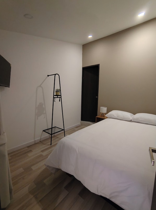 A hotel room with a bed, a nightstand, a lamp, a black metal shelf with plants, and a door. - An des 97 Guest House (Bogotá)