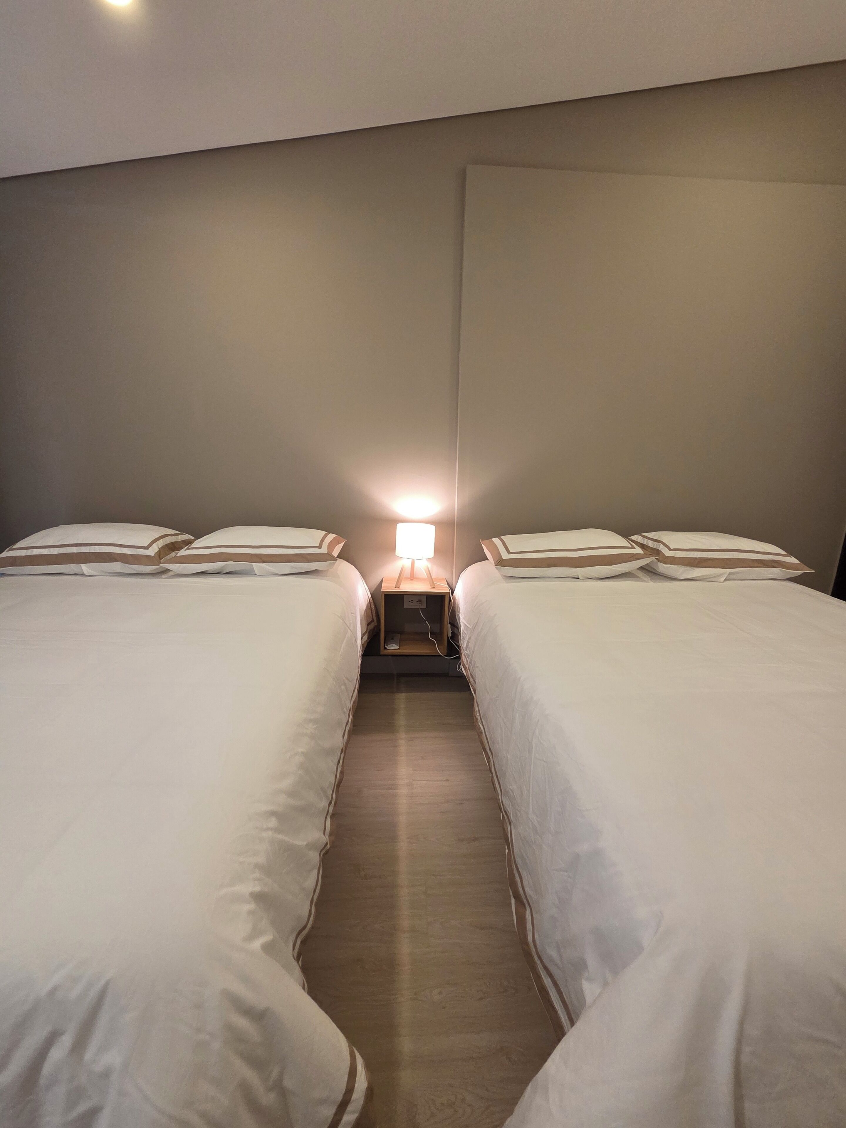 Ein Hotelzimmer mit zwei Einzelbetten, einem Nachttisch mit Lampe und Holzboden.