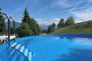 Piscina com escada de metal, rodeada por árvores e vista para montanhas.