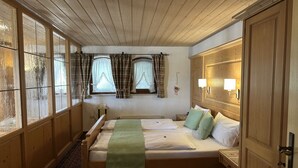 Habitació amb un llit gran, un armari de fusta, una finestra amb cortines i una làmpada penjada a la paret.