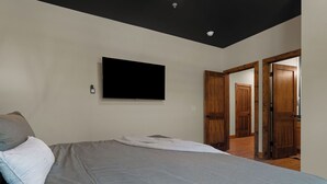 Ein Schlafzimmer mit einem Bett, einem flachbildfernseher an der Wand und einer Tür zu einem weiteren Raum.