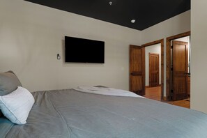 A bedroom with a bed, a flat-screen TV mounted on the wall, and a door leading to another room. - Resort Pools & Lazy River | 6BR Sleeps 14 (Hollister)