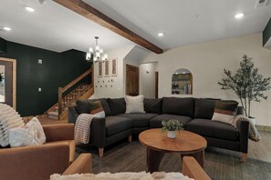A modern living room with a sectional sofa, a wooden coffee table, and a staircase leading to another level. - Resort Pools & Lazy River | 6BR Sleeps 14 (Hollister)