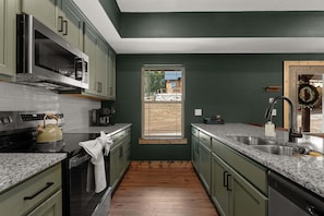 Cozinha com armários verdes, uma janela e vista para um edifício.