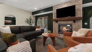 Ein modernes Wohnzimmer mit Kamin aus Stein, bequemen Sitzgelegenheiten und einem großen Flachbildfernseher an der Wand.