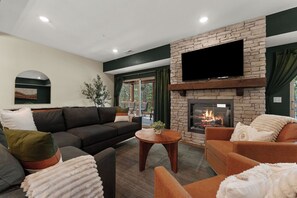A modern living room with a stone fireplace, comfortable seating, and a large flat-screen TV mounted on the wall. - Resort Pools & Lazy River | 6BR Sleeps 14 (Hollister)